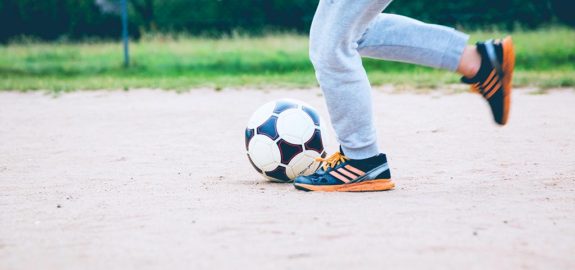 The feet of someone kicking a soccer ball