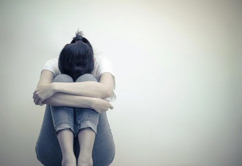 A women sits with her legs bent and her head between her knees.